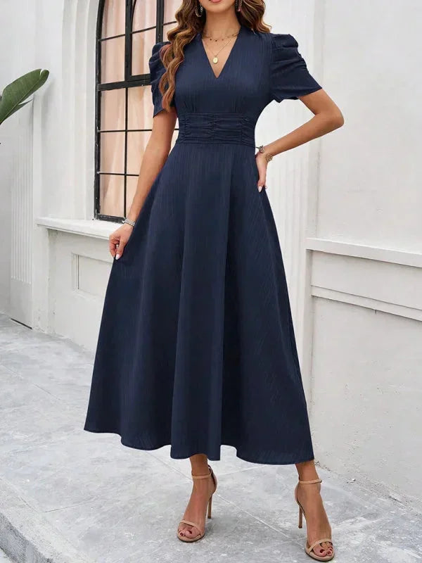 Woman wearing a navy blue dress standing against a white wall.