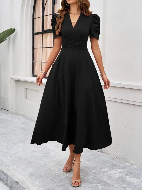 Woman wearing a black dress standing in front of a white building.