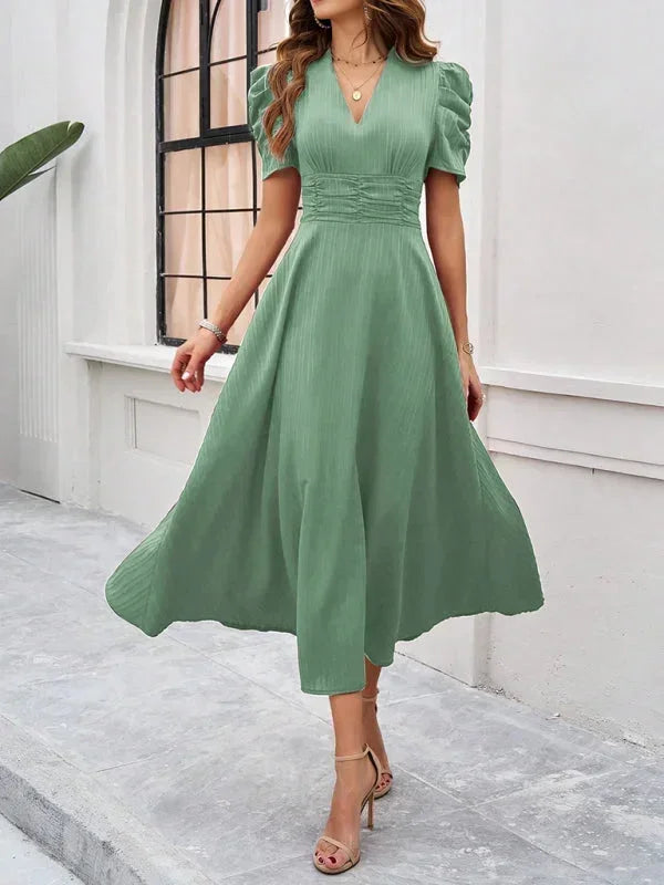 Woman wearing a green dress standing in front of a white wall.