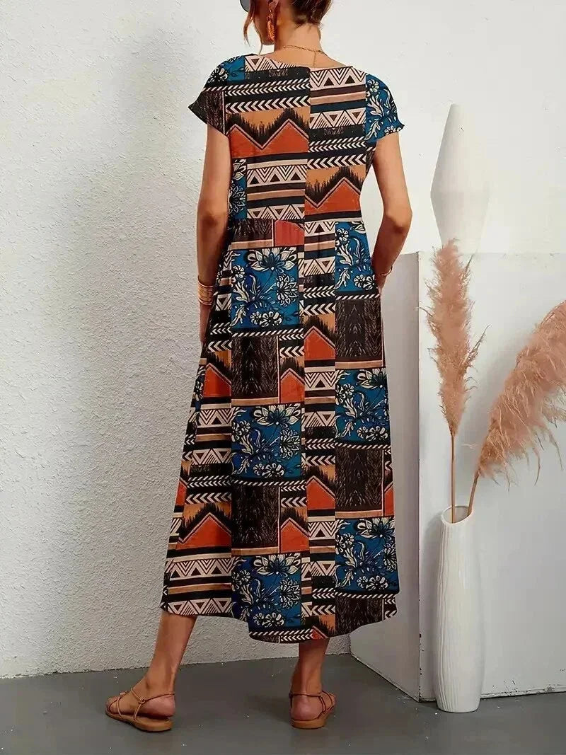 Woman wearing a long, patterned dress against a white wall.