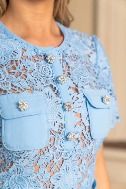 Close-up of a blue lace dress with floral embellishments on a blurred background