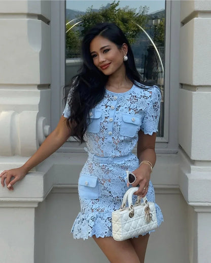 Woman in a light blue lace dress holding a white handbag against a building background