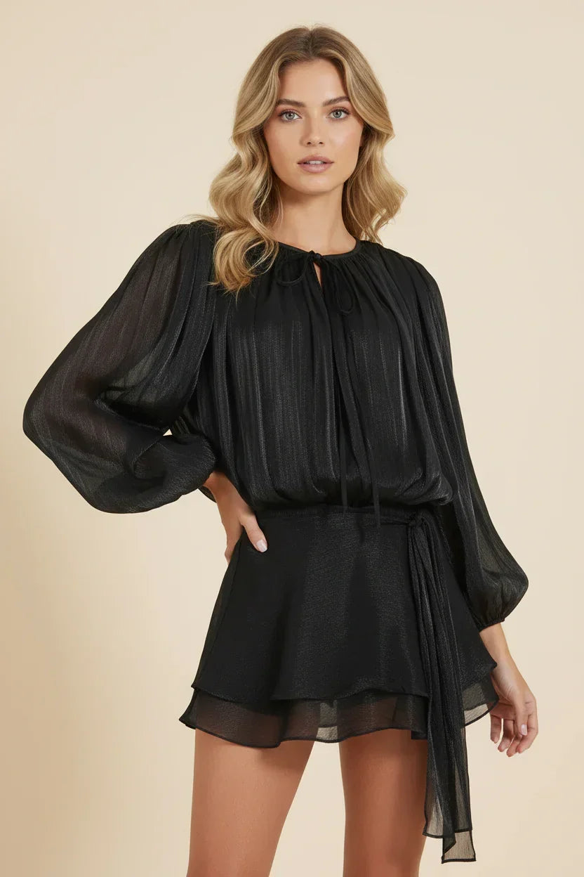 Woman wearing a black dress with sheer sleeves on a beige background