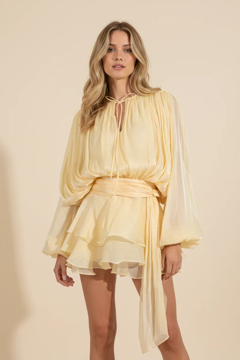 Woman wearing a yellow dress with a sheer overlay on a beige background