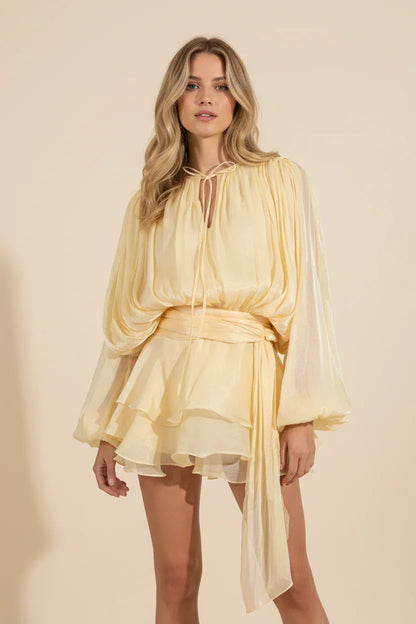 Woman wearing a yellow dress with a sheer overlay on a beige background