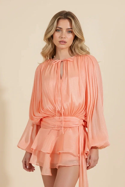 Woman wearing a peach-colored dress with long sleeves on a beige background