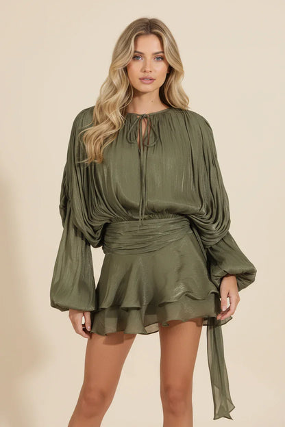 Woman wearing an olive green dress with long sleeves on a beige background