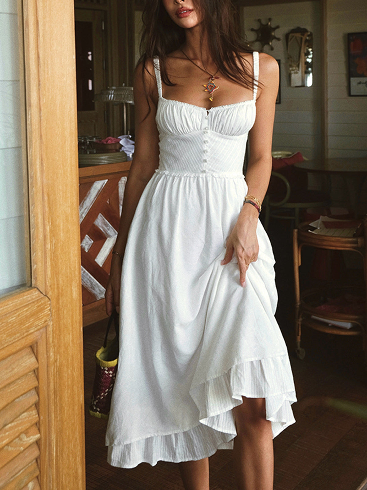 Woman wearing a white dress standing in a room with wooden furniture.