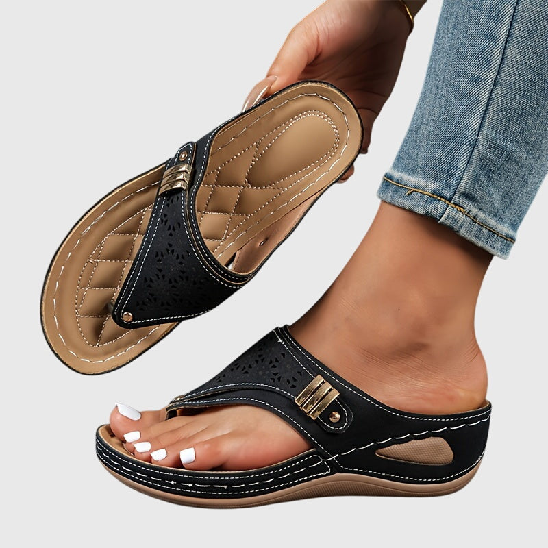 Black sandals with gold accents worn by a person on a light gray background