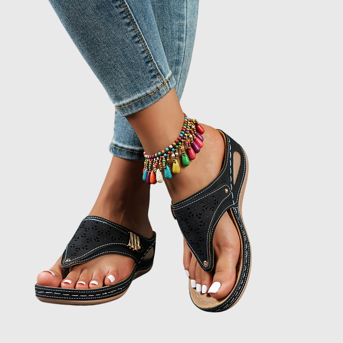 Black sandals worn with colorful anklets on a light gray background