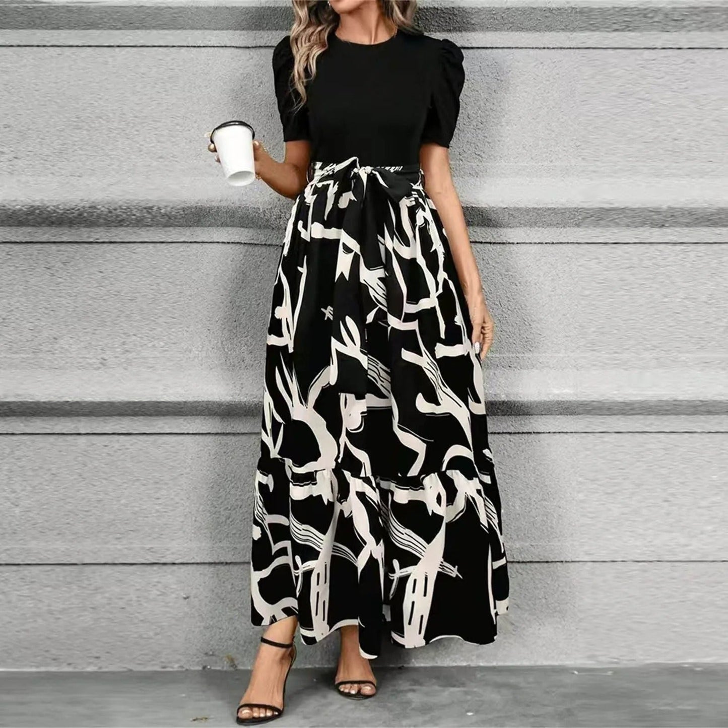 Woman wearing a black top and a long black and white patterned skirt against a gray background.
