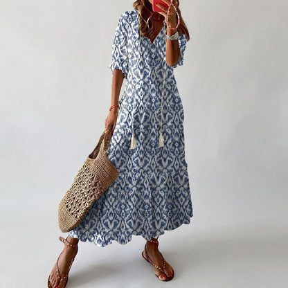 Woman wearing a blue patterned dress holding a woven bag against a plain background
