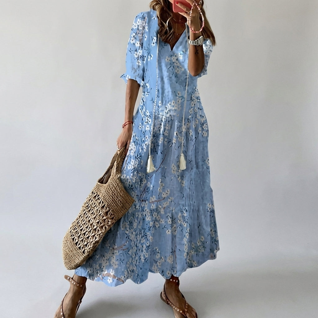 Person wearing a blue floral dress holding a woven bag against a plain background